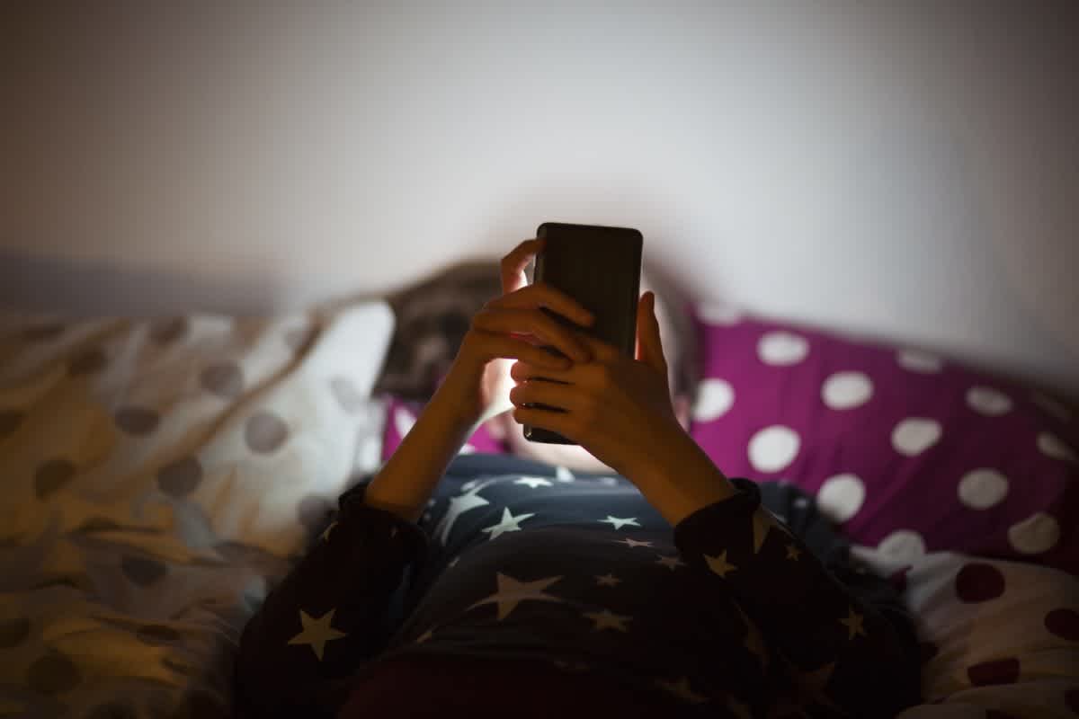 Child in their bedroom at night using an iphone to chat with an AI chatbot.