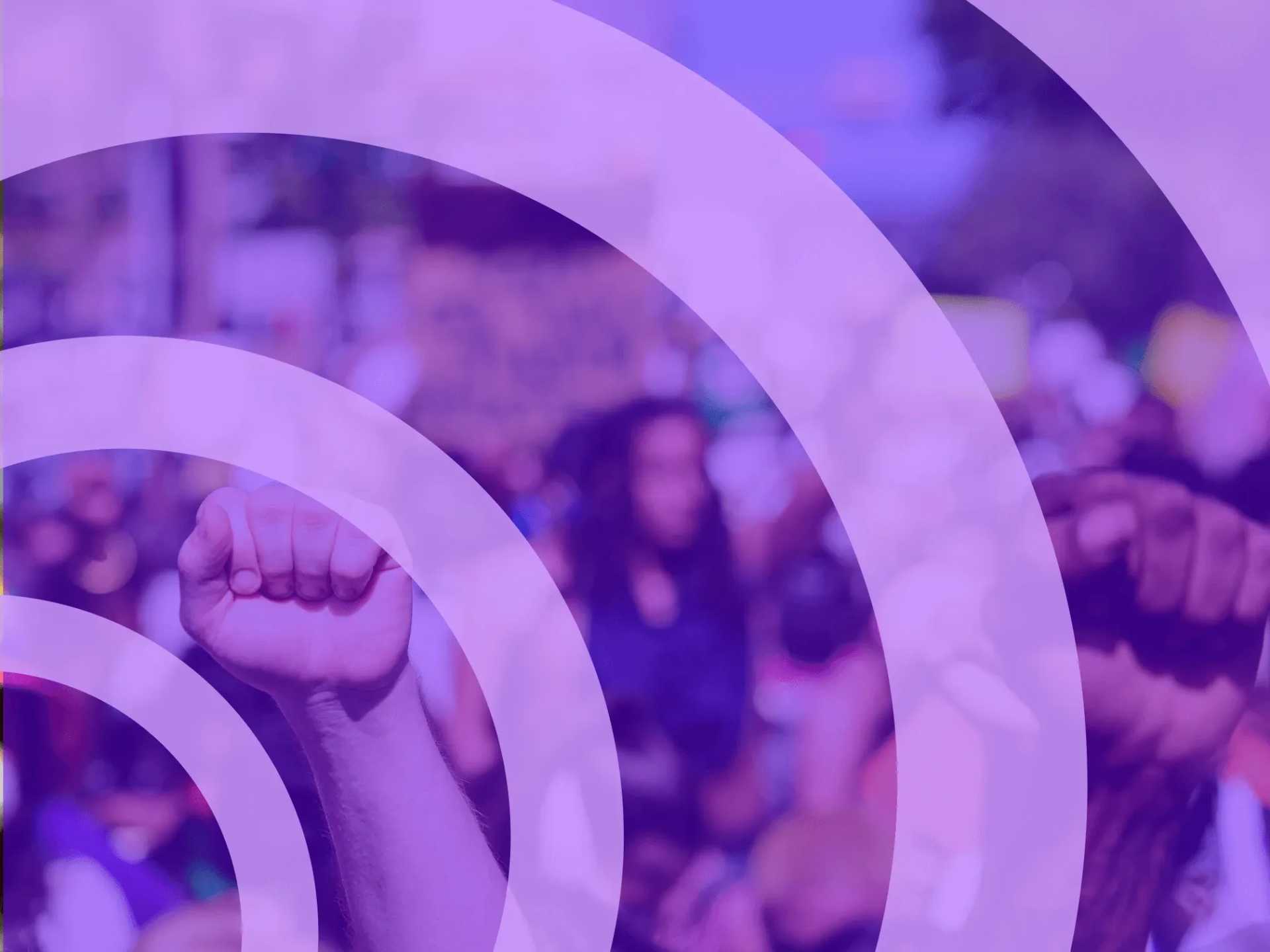 The image depicts a crowd of people protesting, with a raised fist visible among them.