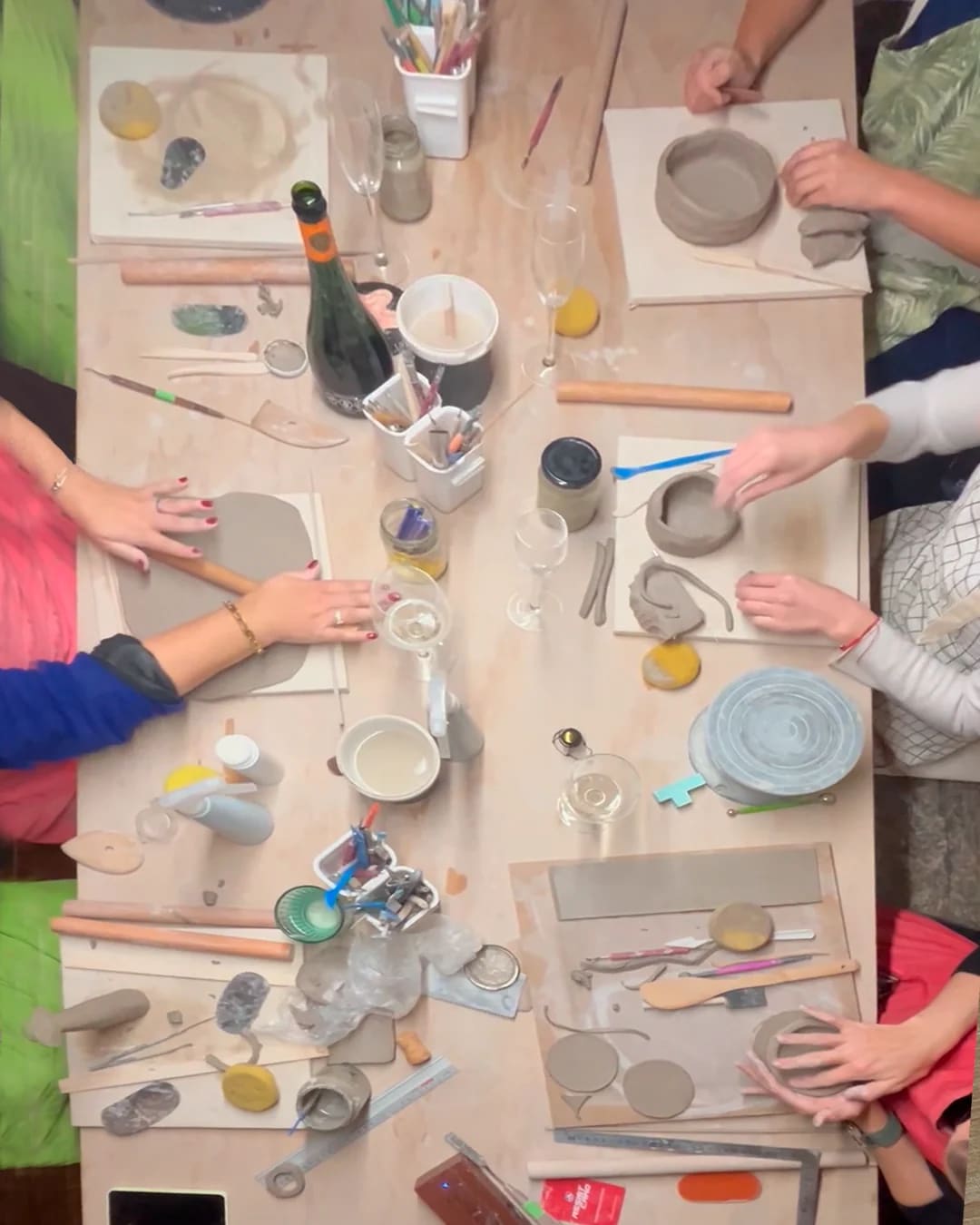 Taller de cerámica con materiales sobre una mesa de madera, con manos trabajando