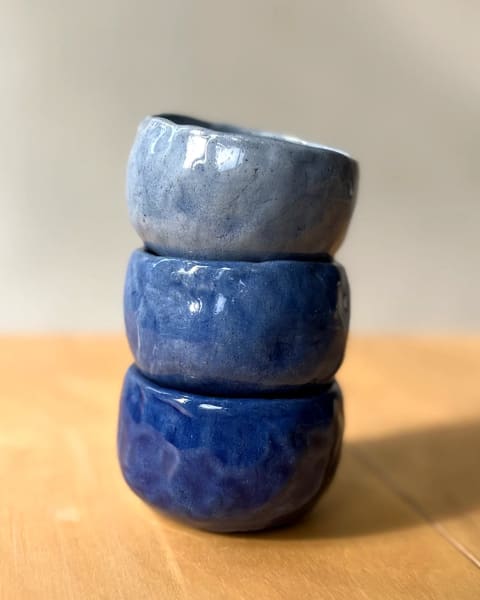 Tres pocillos de cerámica en distintos tonos de azules apilados sobre una mesa de madera