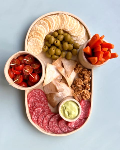 Una bandeja de cerámica para picoteo con galletas, aceitunas y salame
