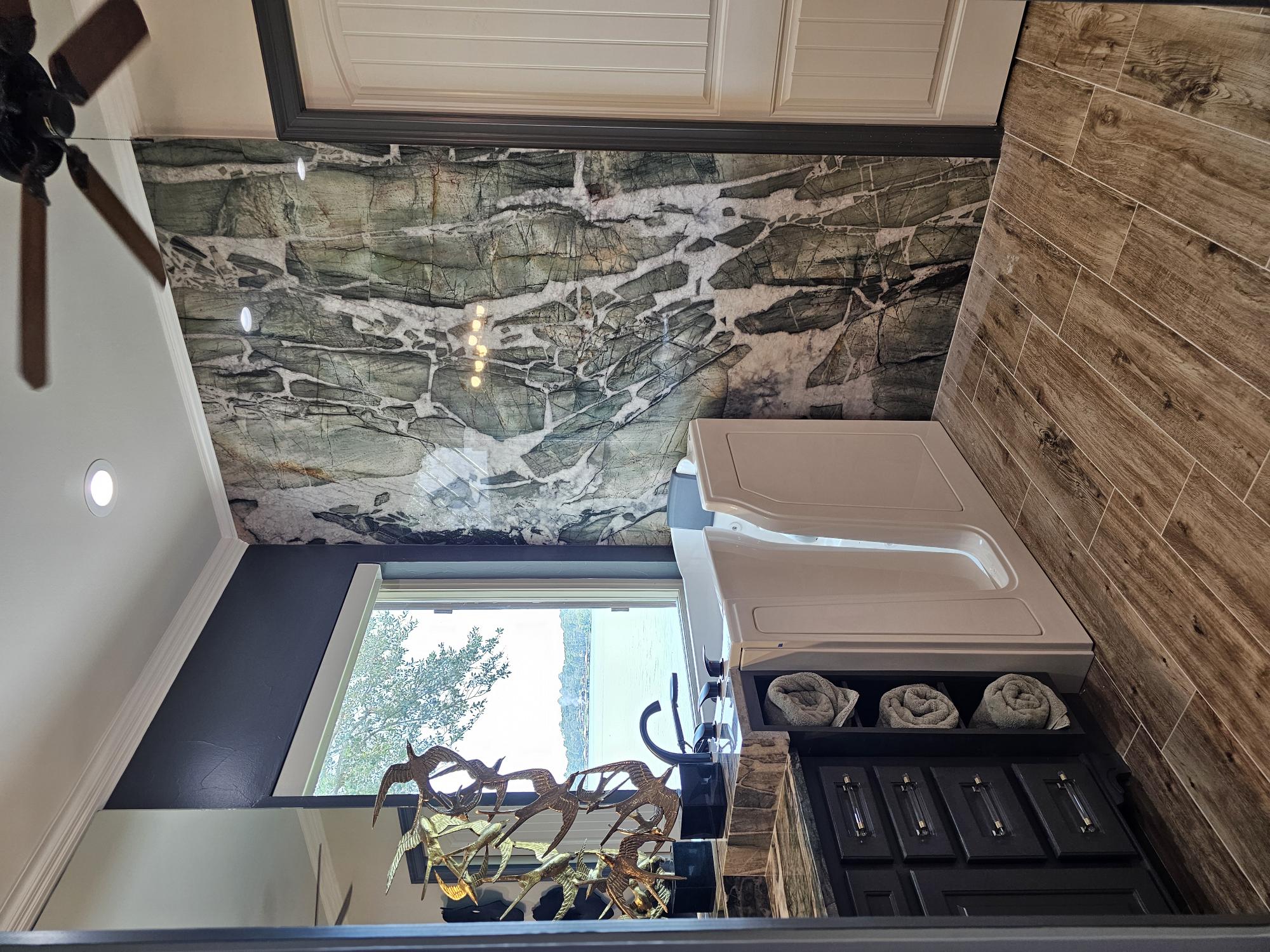 Luxurious bathroom featuring a striking granite backsplash, elegant walk-in tub, dark cabinetry, and natural wood flooring, enhancing the space's depth and texture.