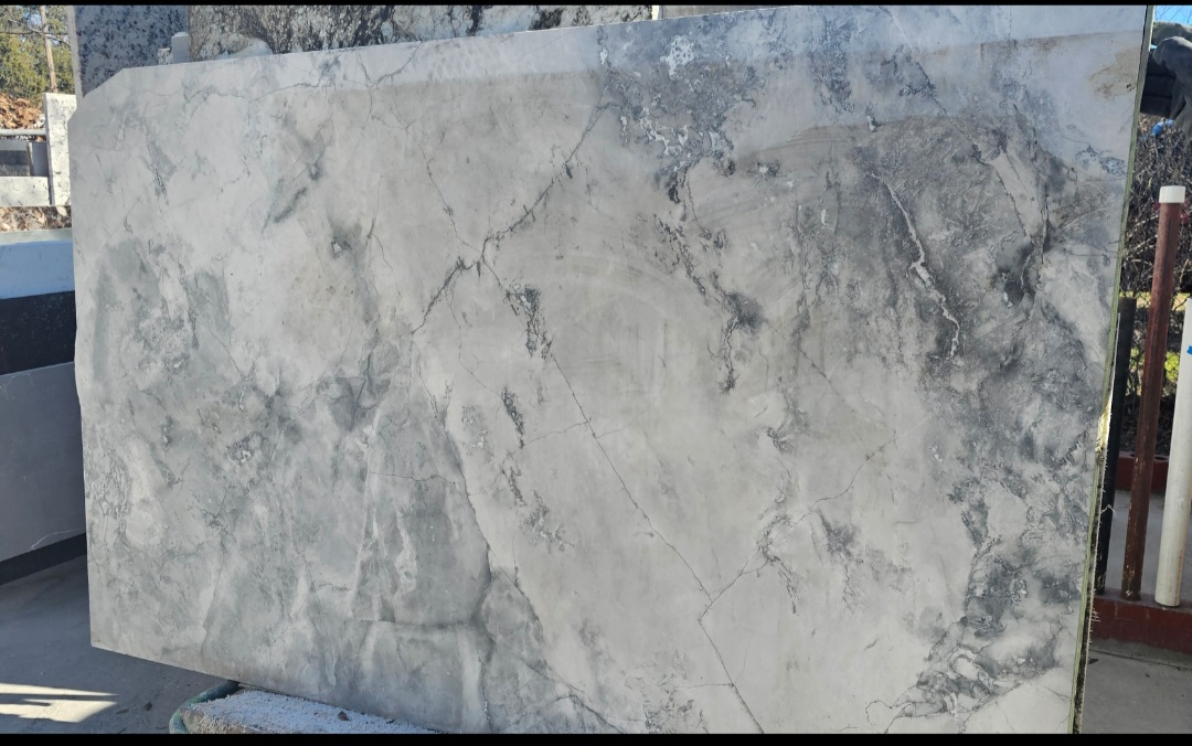 Full slab of marble showcasing intricate veining and tonal variations, displayed in a stone showroom setting for client selection.