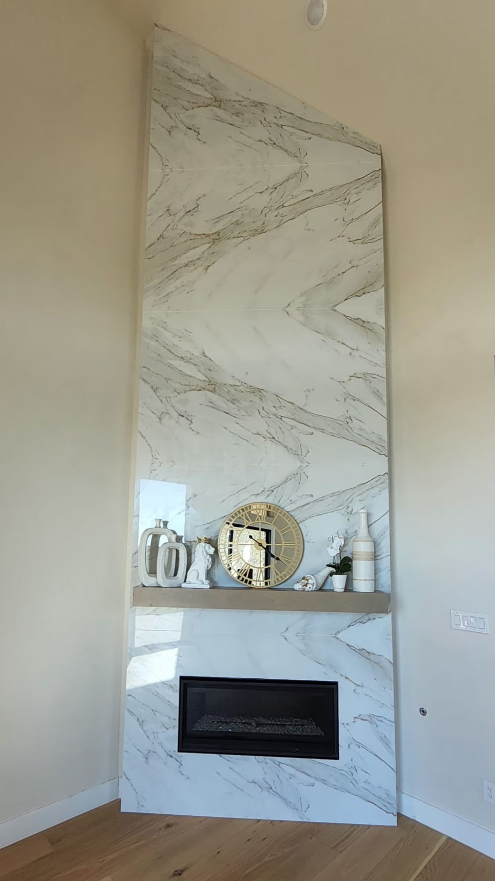 Modern fireplace featuring porcelain and sintered stone cladding with marble-like patterns, decorative shelf with a clock and vases, showcasing durability and aesthetic appeal for contemporary interiors.