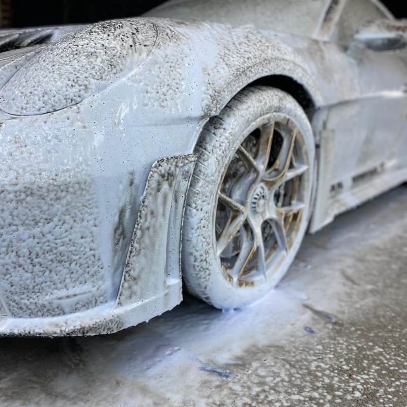 Porsche 911 grise en prélavage snow foam — focus jante avant et flanc carrossé