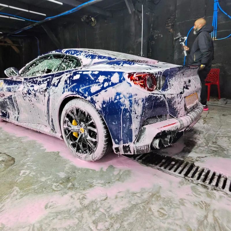 Ferrari bleu nuit sous snow foam — vue 3/4 arrière et étriers céramique jaunes