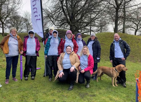 A group of people wearing sweatshirts poses outdoors with a dog.