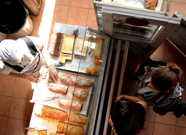 A baker prepares pastries while customers observe in a bright bakery.