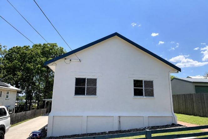 Freshly painted rendered brick home exterior in crisp white with dark roof trim. Residential exterior painting completed by Blue Collar Painting, Gold Coast.