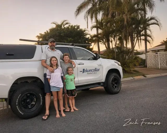 Local painter Zach Fransen standing with his children beside a branded Blue Collar Painting work vehicle at sunset in the Gold Coast