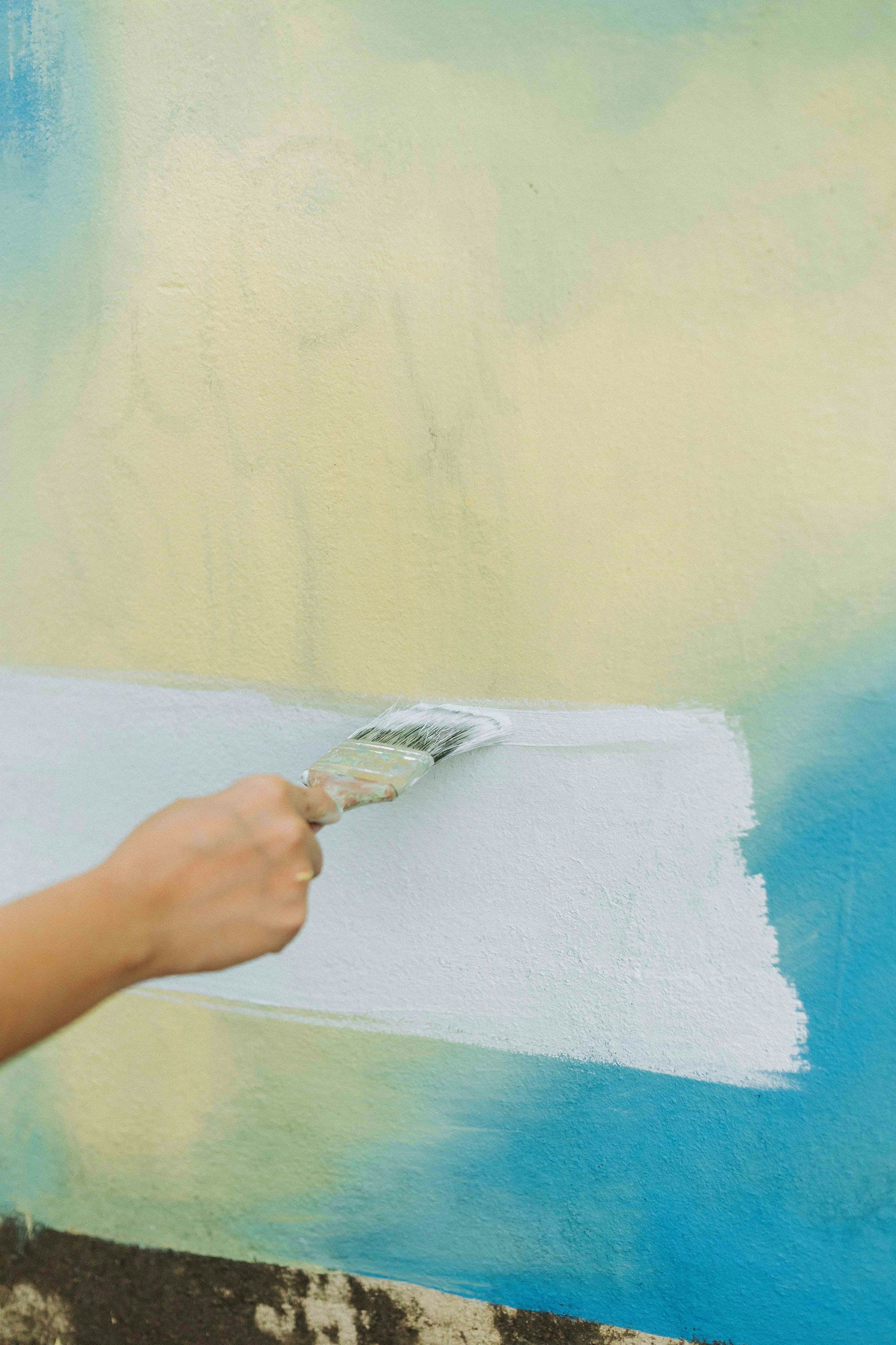 Close-up of a painter's hand applying white paint with a brush — demonstrating the careful prep and quality finish Blue Collar Painting delivers on every job