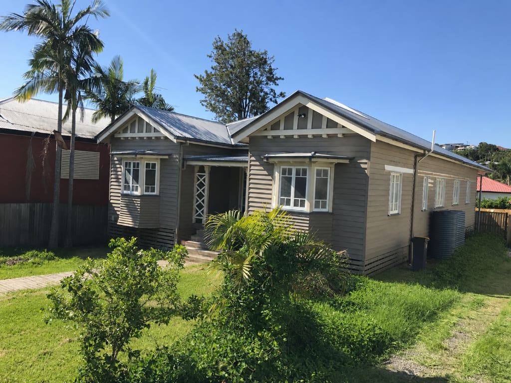 Freshly painted weatherboard Queenslander home exterior in warm taupe with white window frames and timber trim — exterior house painting completed by Blue Collar Painting, Gold Coast
