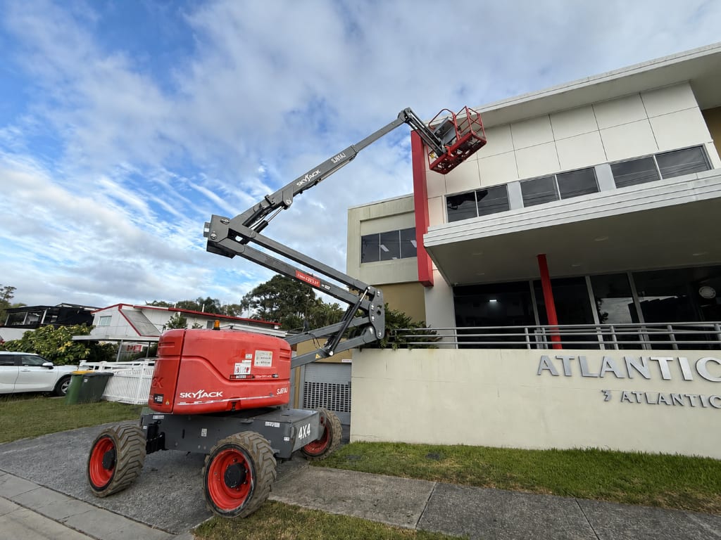 Skyjack 4x4 boom lift extended to the upper storey of the Atlantic commercial building during an exterior painting project — Blue Collar Painting, Gold Coast