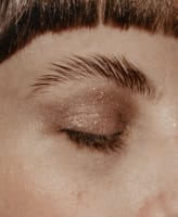 A model's dark pink glittery eye shadow and styled eyebrow