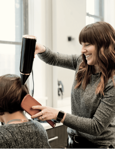 A student brushing and drying a customer's hair
