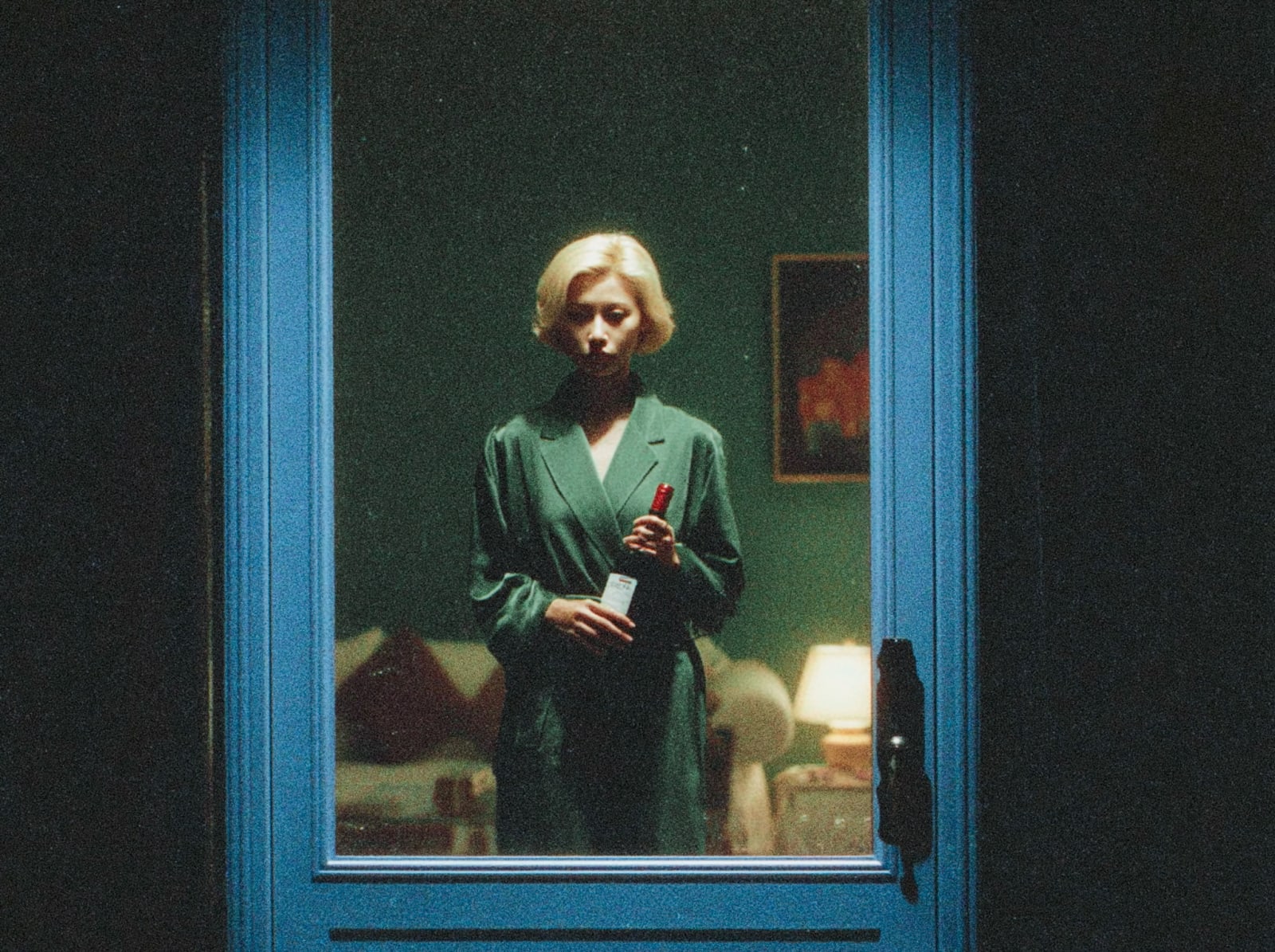 A person standing in front of a blue door holding a bottle, reflected in the door's mirror.