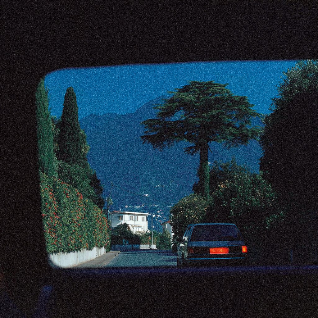 A car parked on a street with trees and a house in the background.