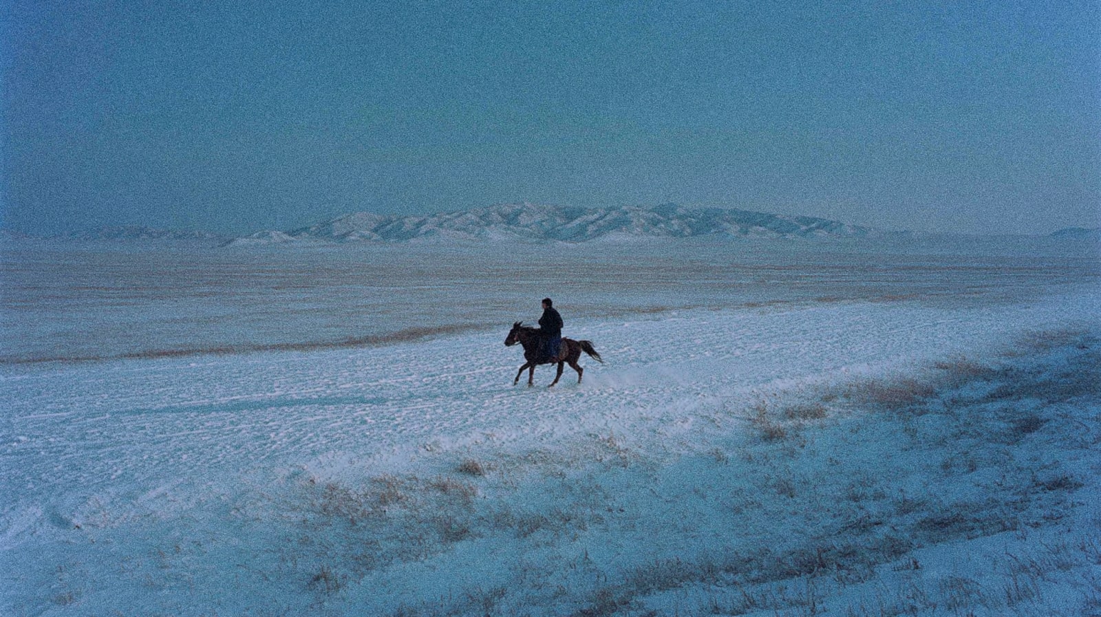 A lone rider on a horse in a snowy landscape with distant mountains.