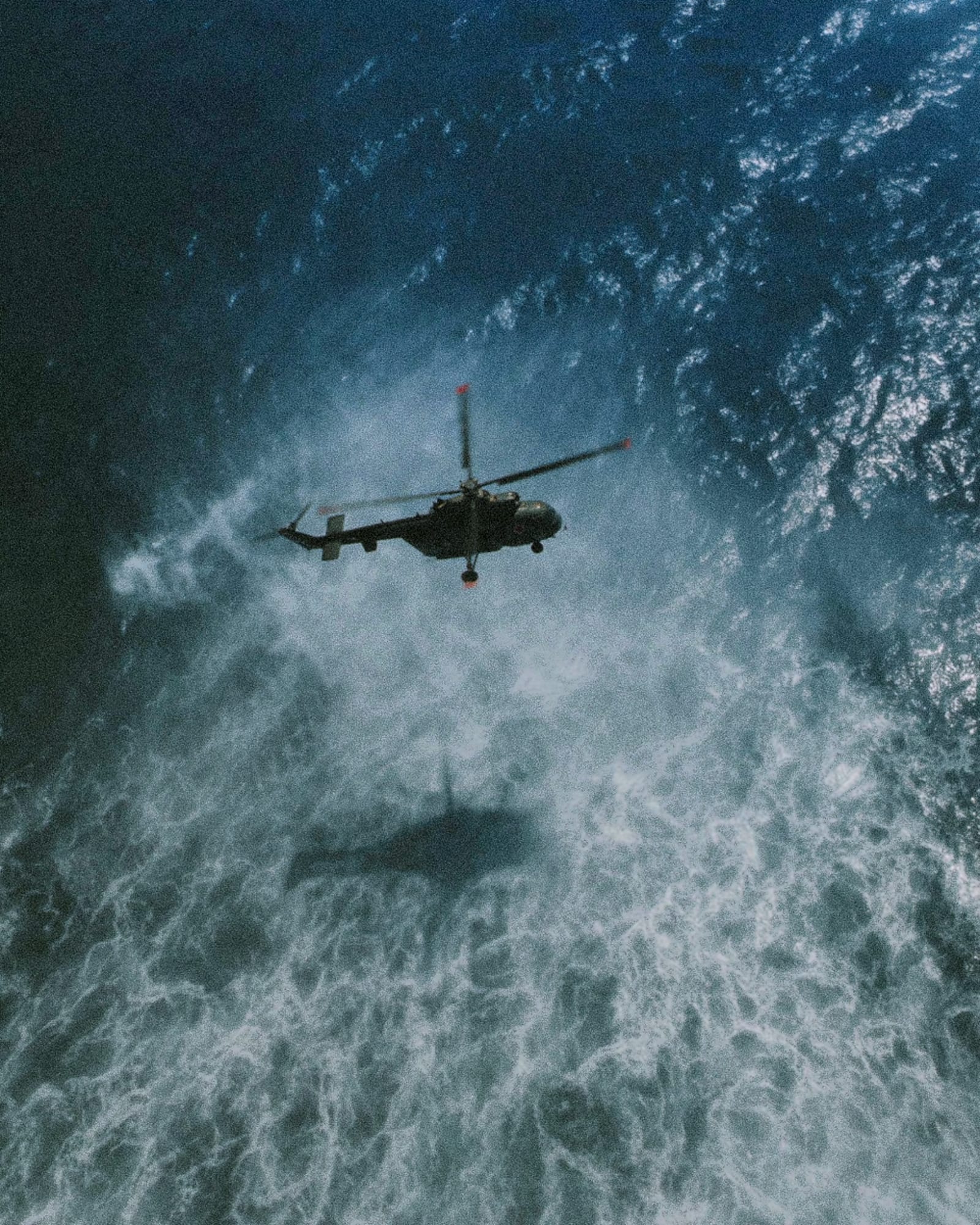 A helicopter flying above turbulent ocean waves.