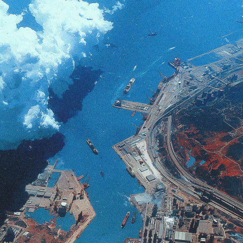 Aerial view of a coastal area with a large body of water and a docked area with ships and cranes.