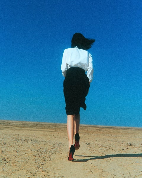 A person walking away from the camera in a desert with a bright blue sky.