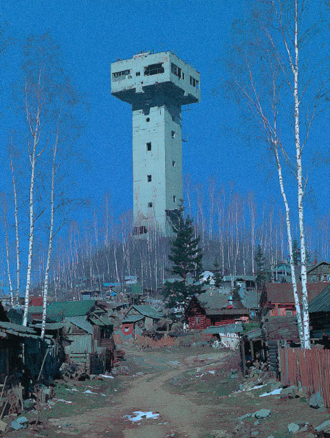 A tall tower with a blue sky and trees in the background.