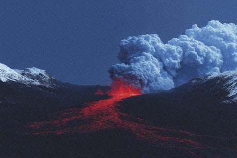 A dramatic volcanic eruption with red-hot lava flowing down the mountain.