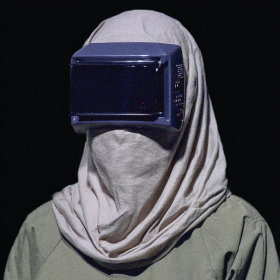 A person wearing a white head covering and a microwave on their head.