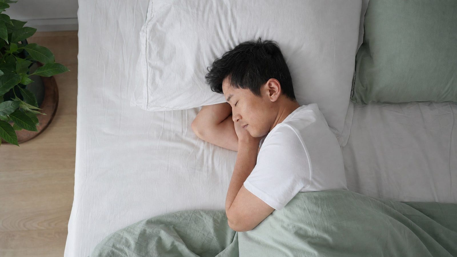 A man sleeps on his side in white and sage green bedding.