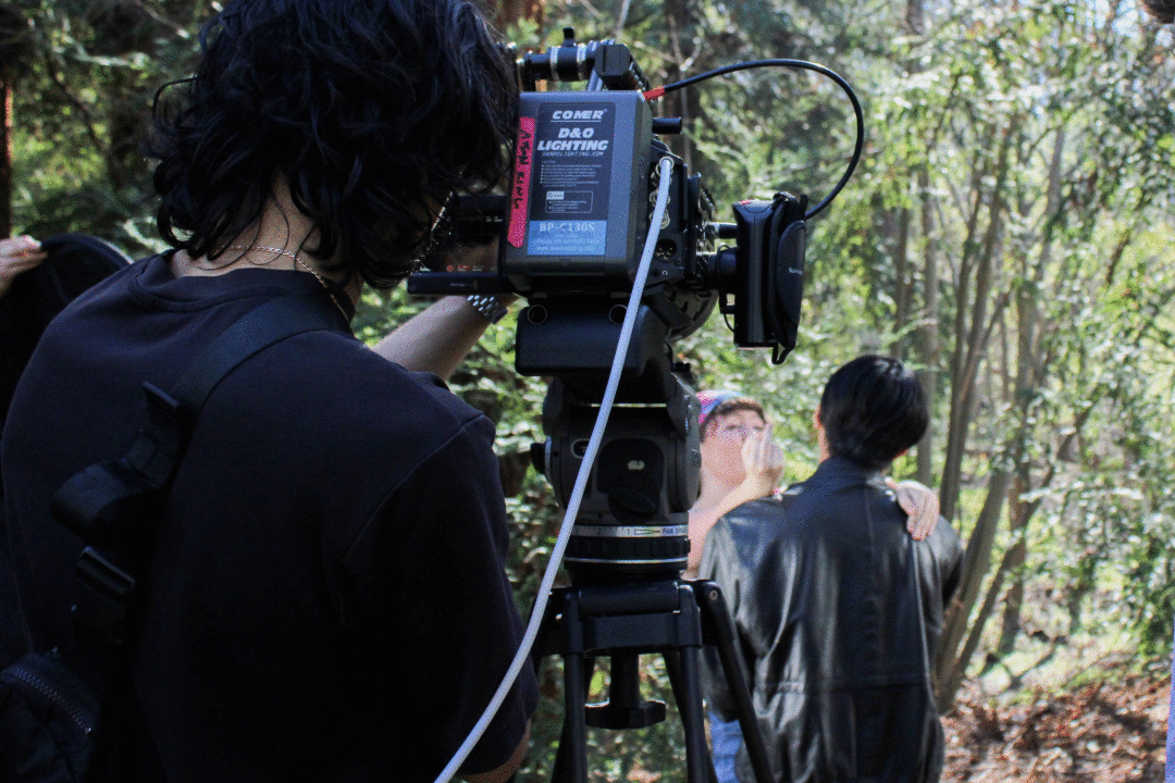 A man looking through a camera pointed at two people