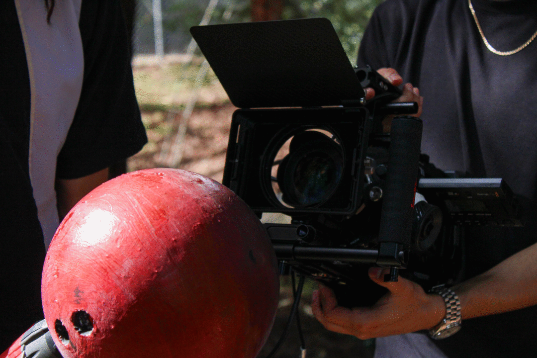 A film camera pointed at a red bowling ball