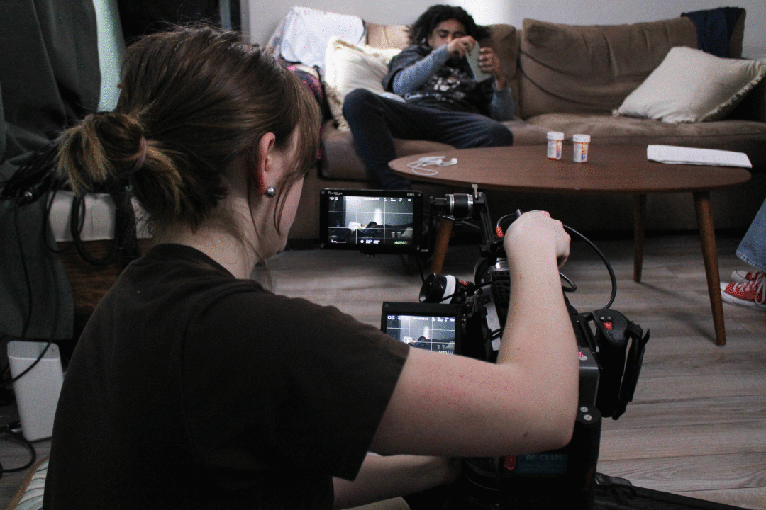 A film camera pointing at someone sitting on a couch