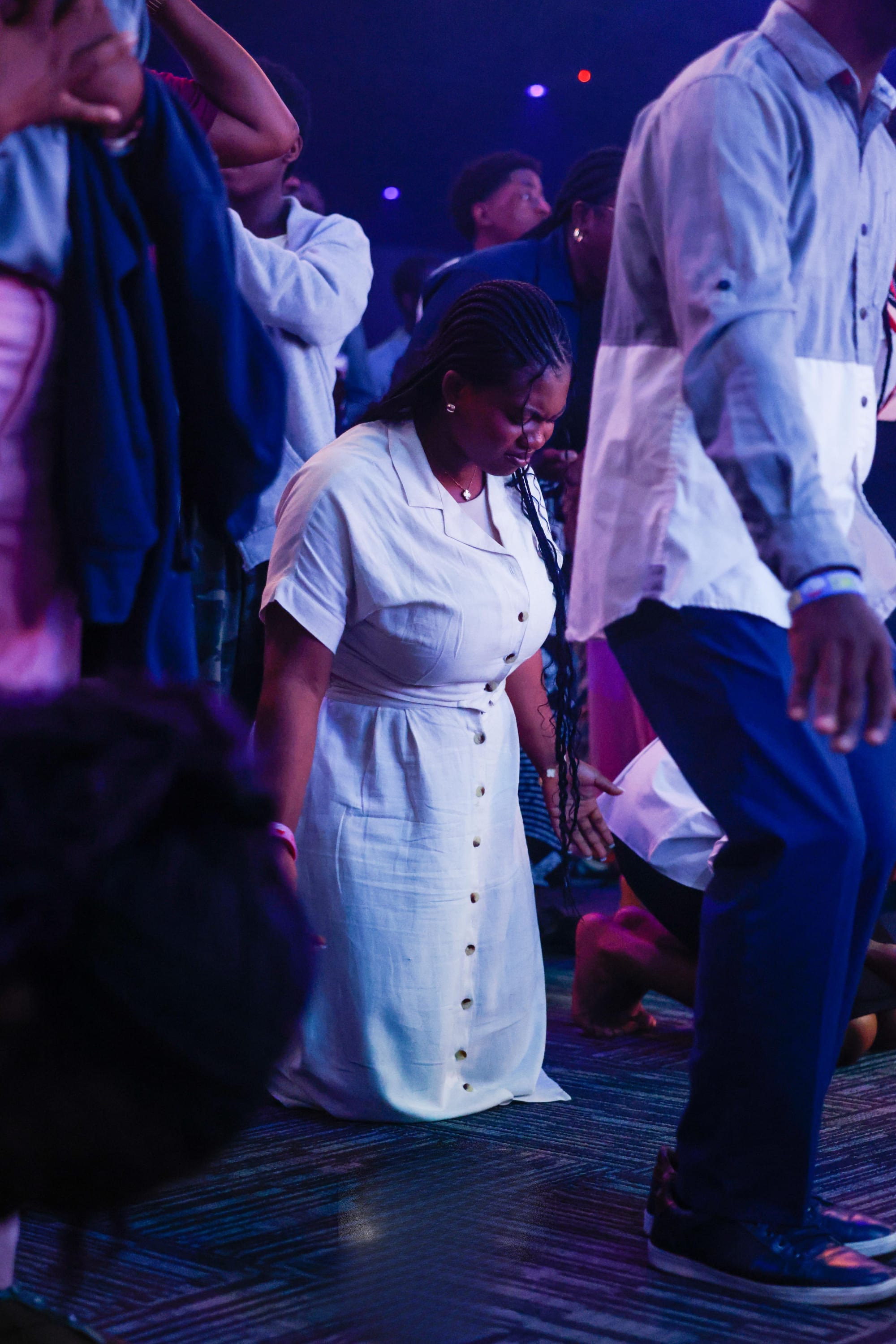 Woman in white dress bowed in worship under stage lights