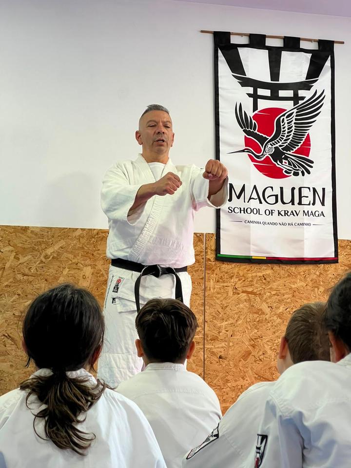 Paulo Parente a explicar uma técnica a um grupo de crianças, com a bandeira da Maguen atrás