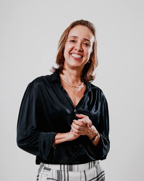 Jaq Priston em pé, sorrindo, com as mãos unidas à frente.