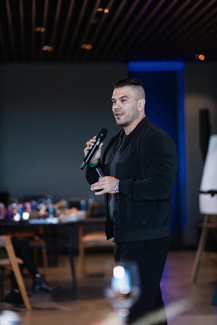 Dr. Rodrigo Schröder falando ao microfone em um evento, de jaqueta preta
