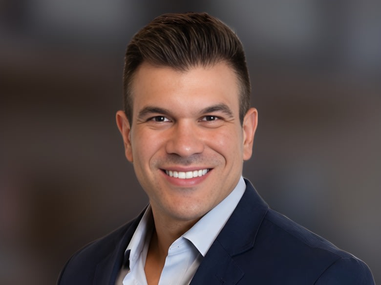 Dr. Rodrigo Schröder sorrindo no consultório, de blazer azul-marinho e camisa azul-clara
