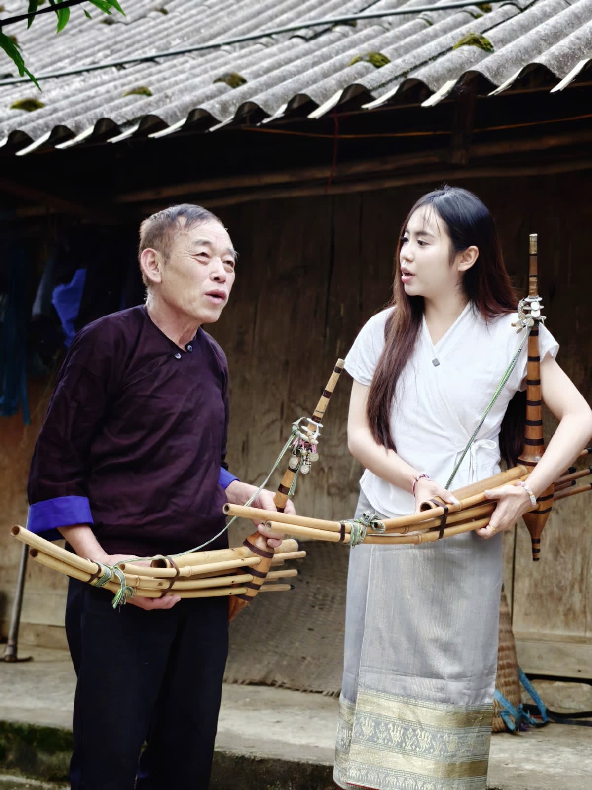 A young woman and a Hmong artisan holding Hmong khèn pipes in Lìm Mông village