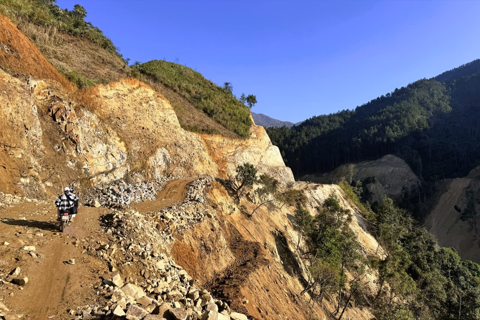 Dirt road into Lùng Cúng hamlet along a cliff, with fallen rocks