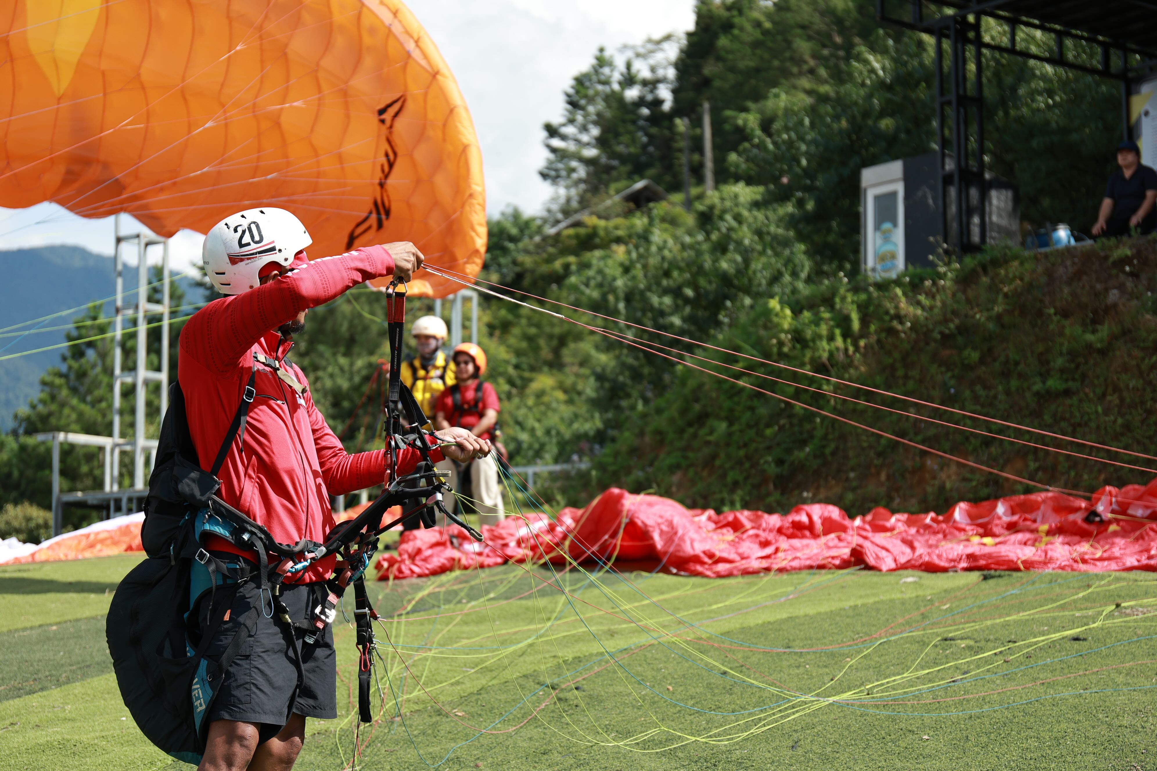A Paragliding pilot checking lines and buckles before launch.