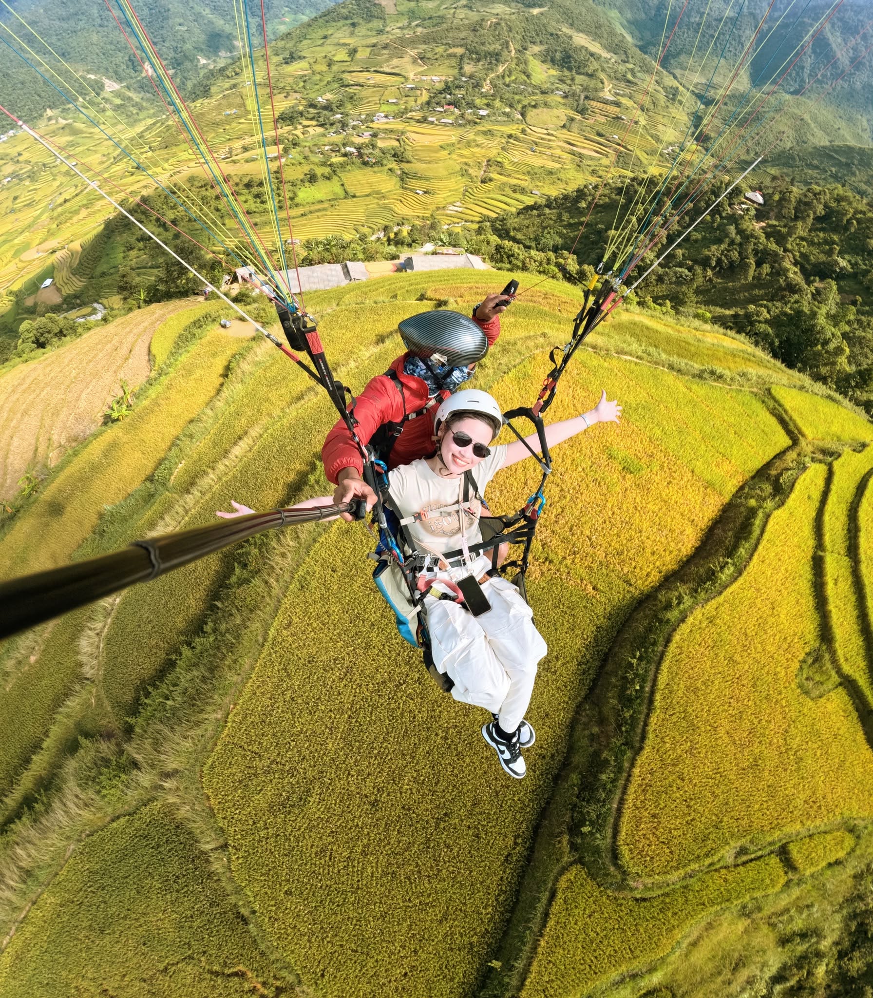 Passenger and pilot flying tandem above golden terraced fields in Sapa