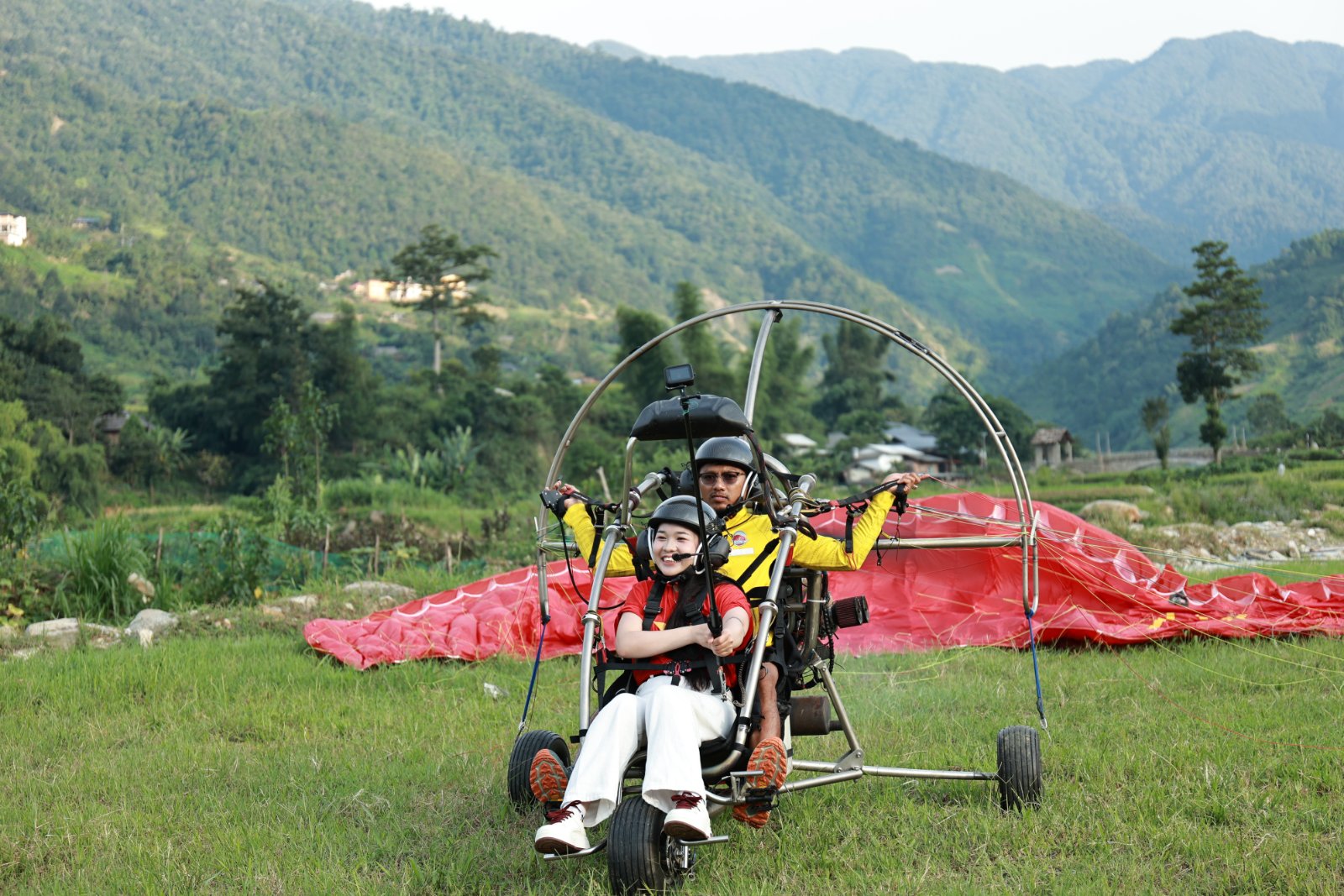Passenger in front, pilot behind, wing laid out — ready to launch from the flat ground below Khau Pha Pass