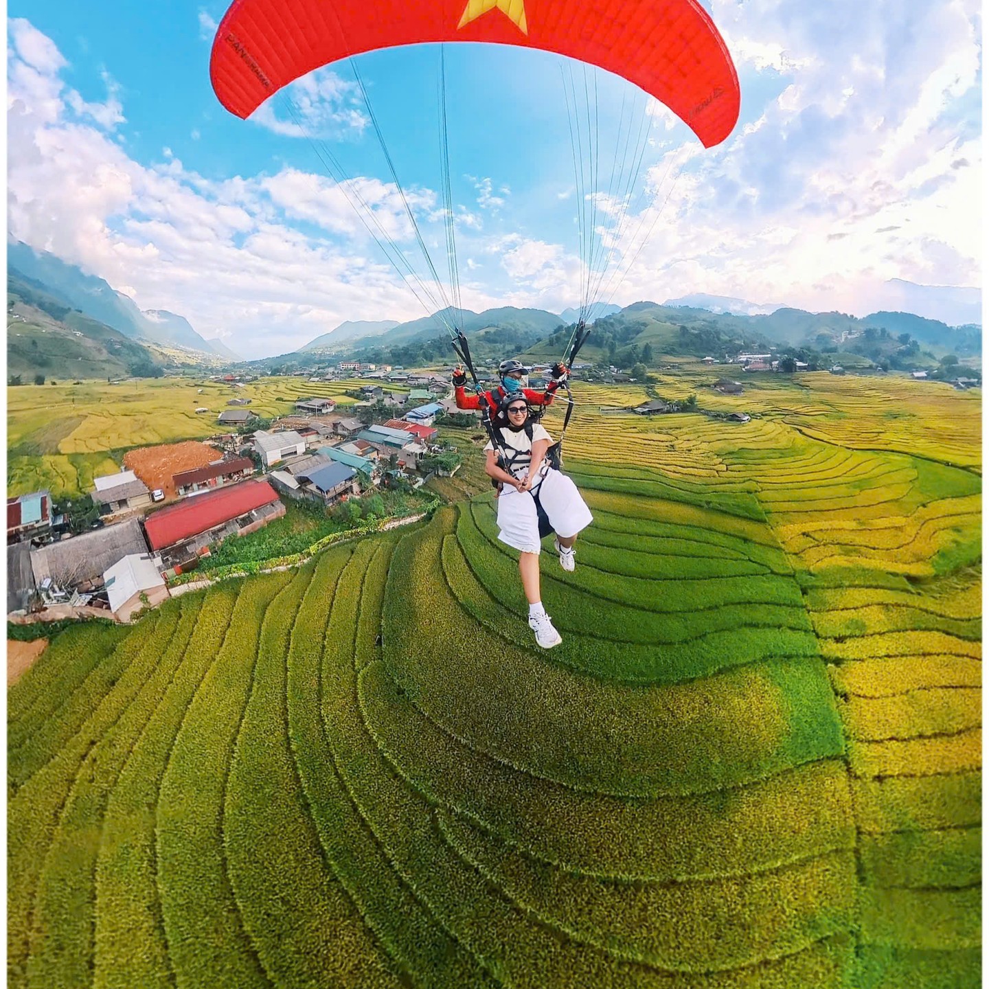 Paraglider in Vietnamese flag colours flying over rice terraces in Sa Pa