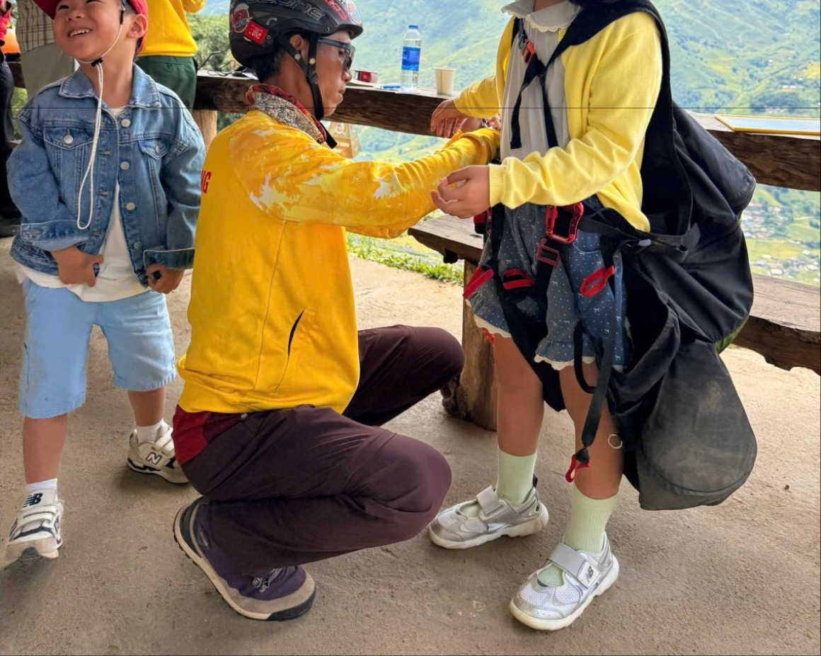 Nhân viên Sapa Paragliding siết dây đùi của đai an toàn cho khách