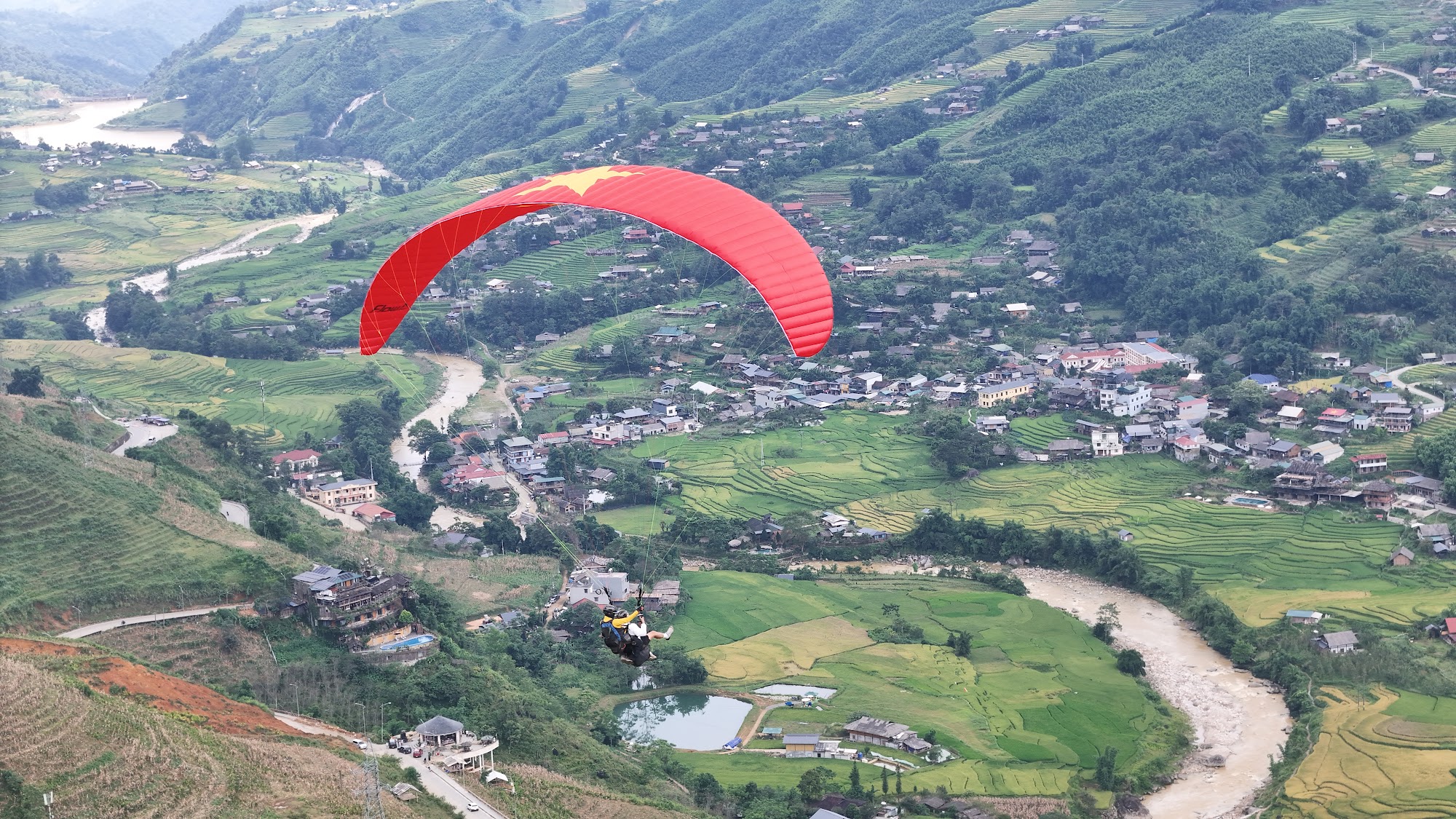 Paraglider with the Vietnamese flag design over Muong Hoa Valley in Sapa