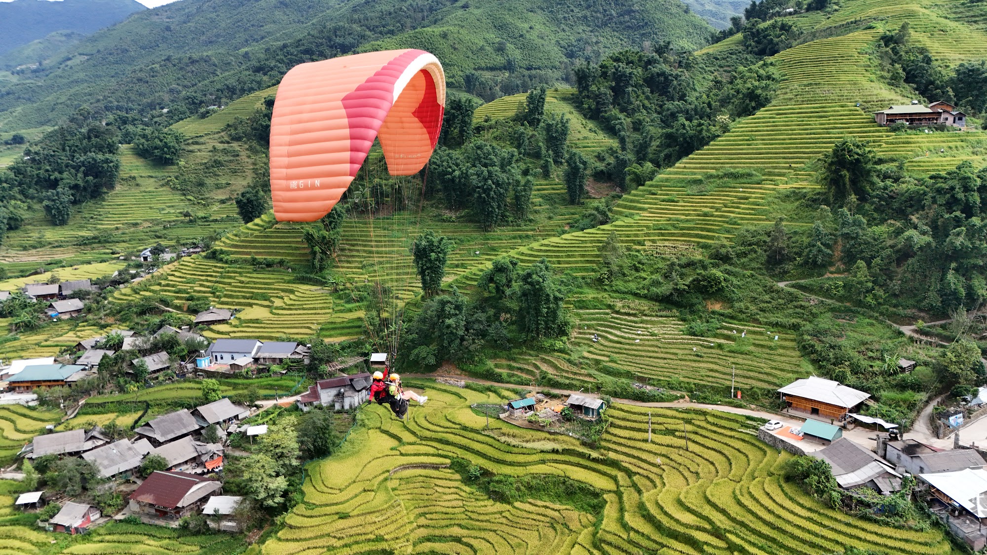 Paraglider flying low over a village and rice terraces in Muong Hoa Valley