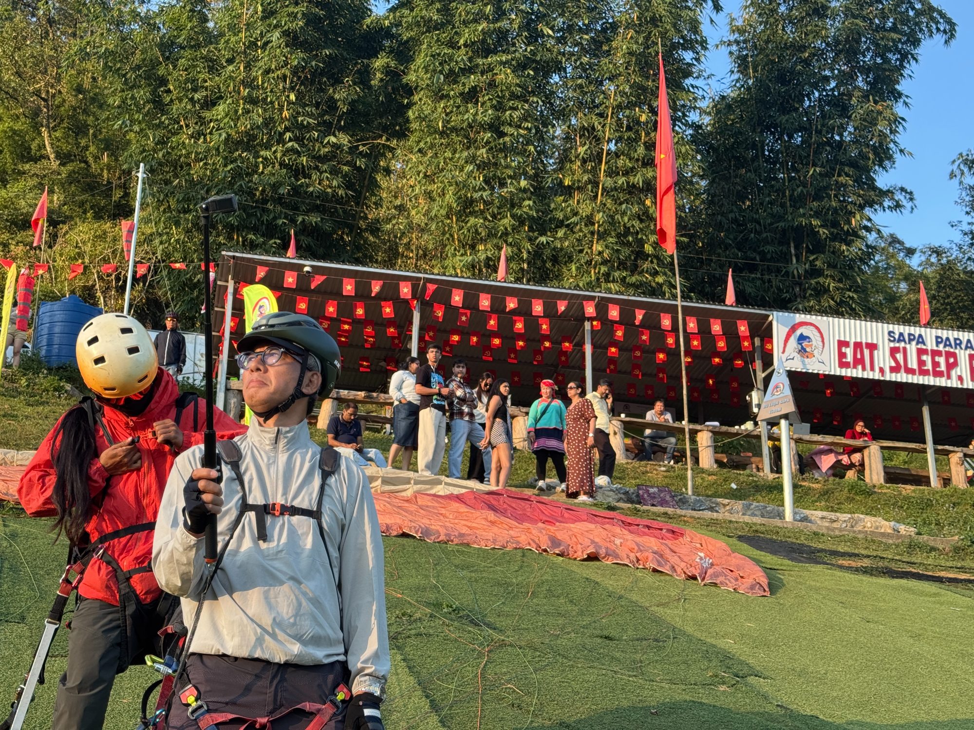 Pilot preparing to launch on the artificial turf with the wing laid out behind and guests watching from the shelter