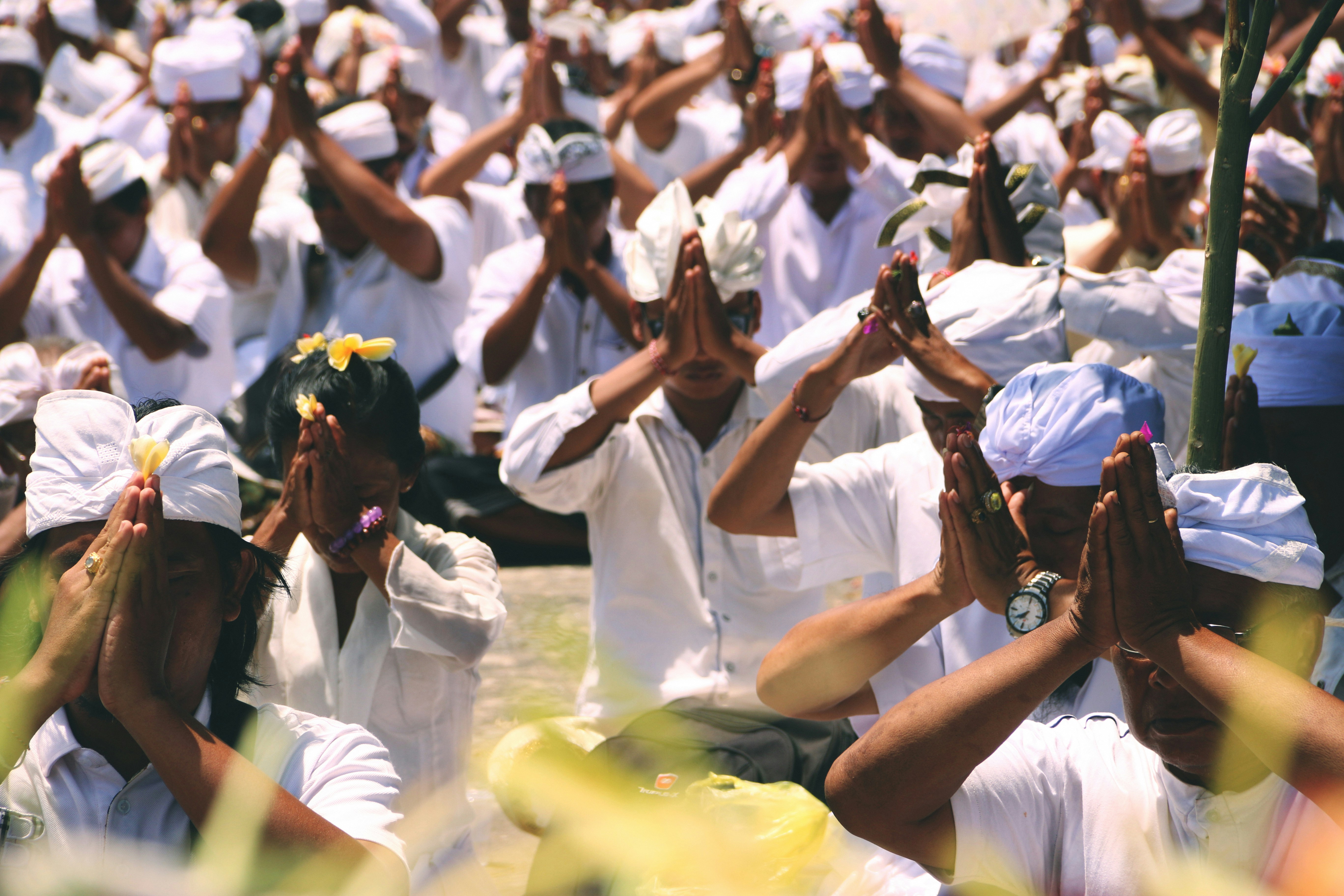 A group of people performing a traditional Balinese offering ceremony, dressed in white with hands in a prayer position.
