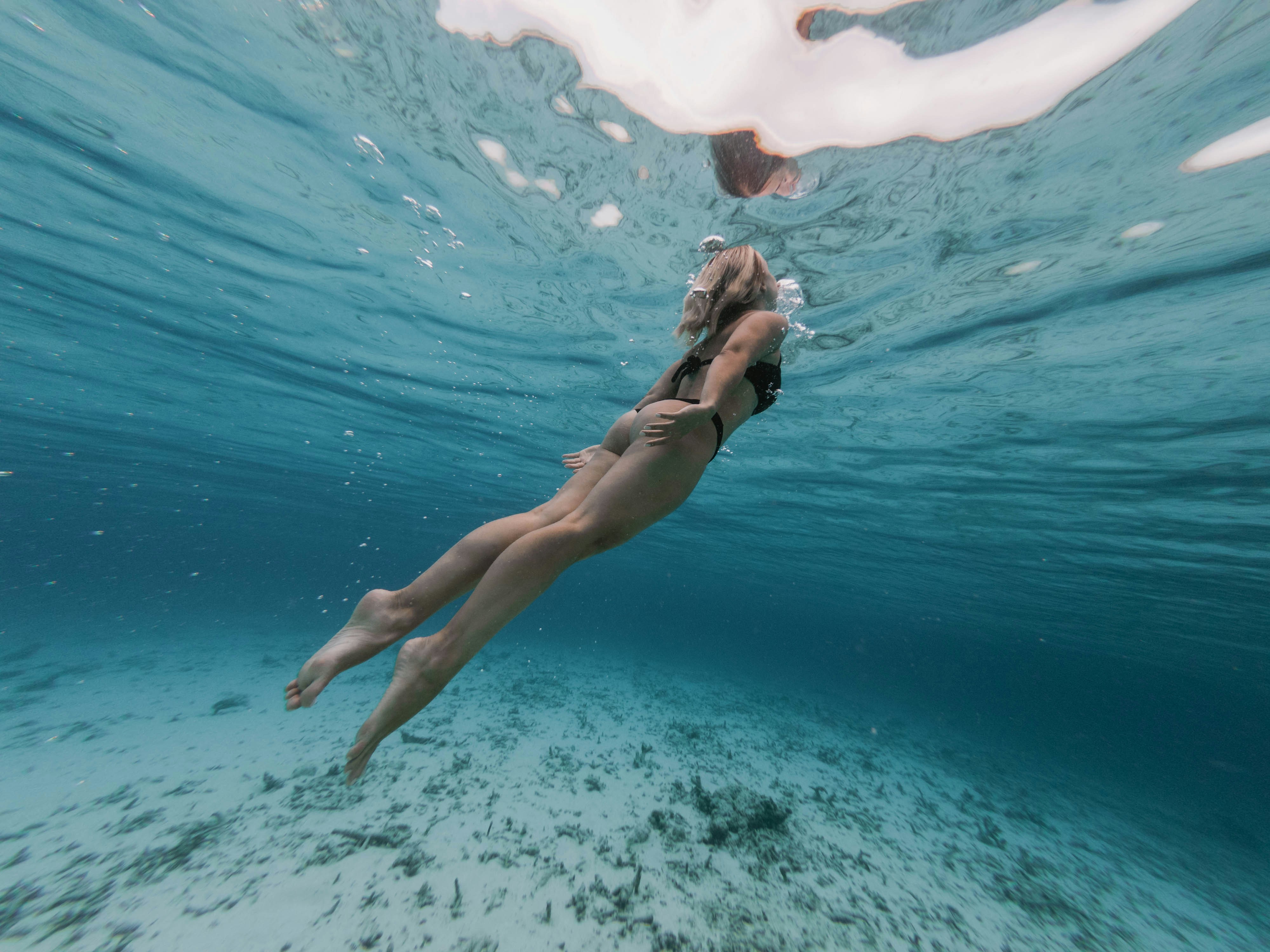 A person swimming gracefully underwater, with the light filtering through the surface and clear waters below