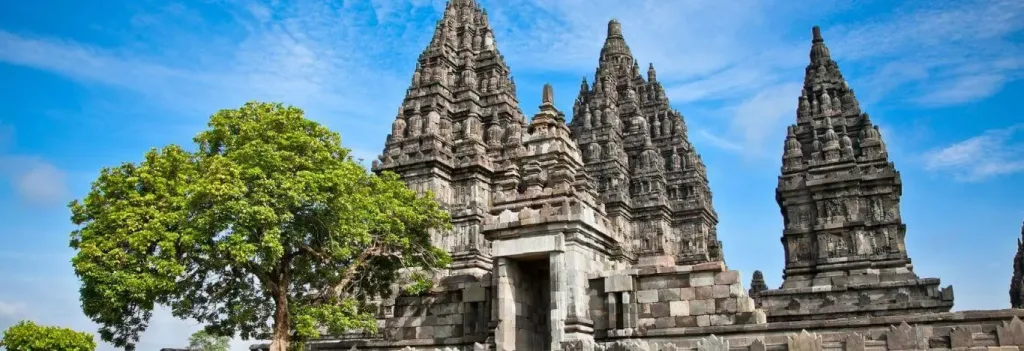 The tall stone spires of Prambanan Temple complex under a blue sky
